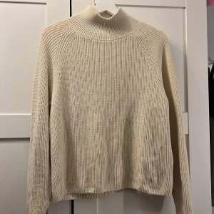Beige stickad polotröja - Snygg beige stickad polotröja med halvpolo och lång ärm. Tröjan har en klassisk rak passform och ribbade detaljer vid hals, ärmslut och nederkant. Perfekt för lager-på-lager under kyliga dagar.