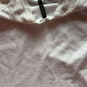 Vit linnetopp med spets från Freequent - Supersöt vit linnetopp från Freequent med smala axelband och v-ringning dekorerad med spets. Toppen är ribbad och har en mjuk, feminin känsla. Perfekt att styla lager på lager eller som den är under varma dagar.