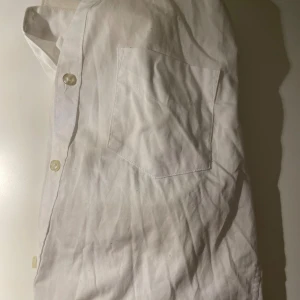 Vit slim fit skjorta från Dressmann - Vit skjorta från Dressmann i slim fit-modell, perfekt för dig som gillar en smalare passform. Skjortan har klassisk krage, knappar framtill och en bröstficka. Tillverkad i mjuk bomull som känns skön mot huden. Enkel och stilren design som funkar till många olika looks.