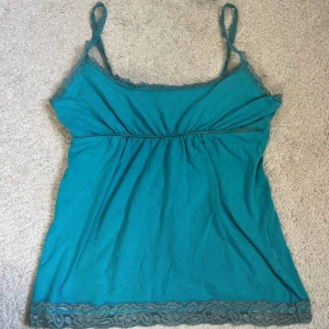 Spets linne - Turkos linnetopp med smala axelband inbyggd bh och dekorativ spetskant upptill och nedtill. Toppen har en lätt rynkad detalj under bysten och är tillverkad i mjuk bomull. Perfekt för dig som gillar 2000s stil och snygga detaljer.💕