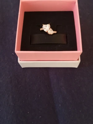 Pandora ring  - Ordinarie pris 1299kr. Helt ny och är helt oanvänd. Med orginal paket. Snygg guldfärgad ring från Pandora med två stora hjärtformade klara stenar i centrum och mindre gnistrande stenar längs bandet. Perfekt för dig som gillar bling och romantiska detaljer. Ringen har en elegant och modern design som verkligen sticker ut.