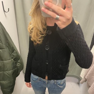 Svart stickad kofta med stora knappar - Säljer en svart stickad kofta med grovt mönster och stora, blanka knappar framtill. Koftan har två små fickor och långärmade ärmar. Perfekt att slänga över en t-shirt eller linne.