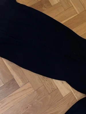 Svart ribbad långklänning NLY Trend - Svart långklänning från NLY Trend i ribbad bomullsmix. Klänningen har knappar framtill och en stilren, figurnära passform som ger en snygg siluett. Perfekt för dig som gillar minimalistisk och modern stil.