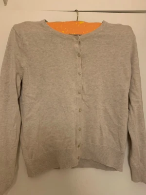 Beige stickad kofta med knappar - En enkel och stilren beige stickad kofta med rund hals och knappar framtill. Koftan har långa ärmar och ribbade muddar vid nederkant och ärmslut. Perfekt att slänga på sig när det är lite kyligt ute. Storleken är S passar även som XS❤️