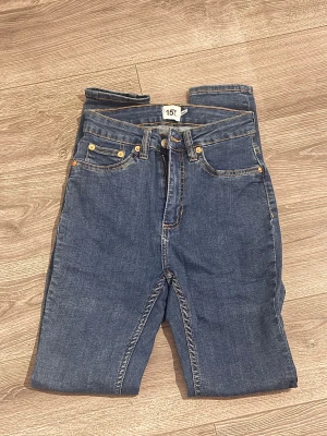 Blå jeans från 157, storlek S - Snygga blå jeans från 157 i klassisk femficksmodell med guldfärgade nitar och dragkedja. Jeansen har normal passform och raka ben, tillverkade i slitstarkt denimtyg med kontrastsömmar. 