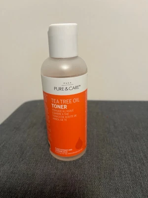 Tea Tree Oil Toner från Pure & Care - Tea Tree Oil Toner från Pure & Care i en genomskinlig plastflaska med vit kork och orange etikett. Tonern innehåller växtextrakt och vitamin B3+E, och är speciellt framtagen för att rengöra och fräscha upp huden samt förbättra hudens elasticitet. Passar perfekt för dig som vill ha en fräsch känsla efter rengöring.