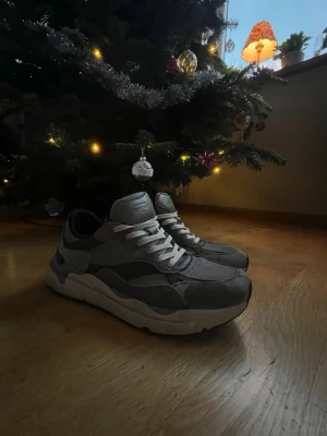 Grå sneakers från GANT, storlek 45 - Säljer ett par snygga GANT sneakers i grått med vita och svarta detaljer. Skorna har en chunky vit sula, snörning och är tillverkade i en mix av mocka, skinn och textil. Perfekt för dig som gillar stilrena och sportiga sneakers med modern vibe.