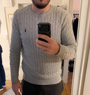 Polo Ralph Lauren tröja S - Säljer en grå kabelstickad tröja från Polo Ralph Lauren. Tröjan har rund halsringning, ribbade muddar och det klassiska broderade logot på bröstet. Perfekt för lager på lager under höst och vinter. Superskön och stilren vibe. Jättebra skick 10/10. Kan diskutera om priset! 