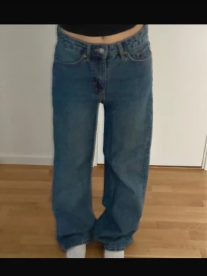 Blå wide jeans från 157, storlek S - Säljer ett par blå jeans från 157 i storlek S. Modellen har en loose och wide/straight passform med klassisk femficksdesign. Jeansen har mid/hög midja och är tillverkade i slitstarkt denimtyg med snygga sömmar och knappstängning framtill.