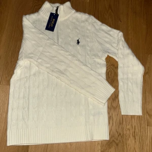 Vit stickad polotröja Polo Ralph Lauren - Säljer en vit stickad polotröja från Polo Ralph Lauren med half zip och klassisk kabelstickad design. Tröjan har lång ärm, ribbade muddar och den ikoniska Polo-loggan broderad på bröstet. Slim fit och riktigt snygg till jeans eller chinos. Är M men passar S eller XS. Helt oanvänd då taggen sitter kvar