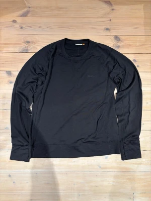 Svart långärmad tröja Lundhags L - Svart långärmad tröja från Lundhags i storlek L. Tröjan har en enkel och clean design med rund hals och diskret logga på bröstet. Materialet känns mjukt och skönt, perfekt för chill dagar eller när du vill ha något basic men snyggt. Tröjan har även öppningar för handvärmare se sista bilden.