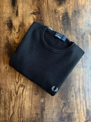 Fred Perry Tröja - Fred Perry tröja i klassisk casuals/old money-stil. Välvårdad och i bra skick utan hål, fläckar eller slitage. Tidlös design med diskret logotyp, stark koppling till brittisk casuals-kultur. Perfekt både till vardag och mer uppklädda outfits. Ett stilrent plagg som aldrig går ur tiden.