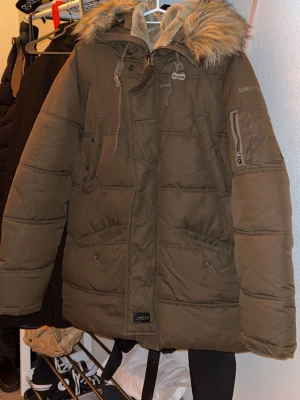 Jacka  - Jacka från Schott NYC med fuskpäls på huvan och flera fickor med dragkedja. Jackan har quiltad design, snörning vid huvan och mjukt foder på insidan. Perfekt för kalla dagar. Skicket är bra då den har använts fåtal gånger. 