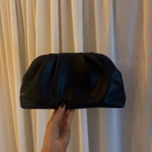 Svart axelväska med kedja - Stilren svart axelväska i skinnimitation med mjuk, puffig form och guld kedja. Väskan har dragkedja upptill och rymligt fack inuti. Perfekt för att bära det viktigaste och ger en trendig touch till din outfit. Funkar även som clutch!❣️