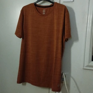 Orange t-shirt från SOC i storlek L - Snygg orange t-shirt från SOC i storlek L. T-shirten har rund halsringning och korta ärmar. Tillverkad i ett lätt och mjukt material som andas, perfekt för träning eller chill. Enkel design utan tryck eller logga på framsidan.