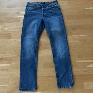 Blå slim fit jeans från Jack & Jones - Snygga blå jeans från Jack & Jones, modell Slim Glenn. Jeansen har klassisk femficksdesign, smal passform och är tillverkade i mjukt denimtyg. Perfekta för dig som gillar en modern och stilren look.   Stl- 29/30