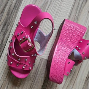 Rosa sandaler med platå och nitar - Säljer ett par coola rosa sandaler med bred platåsula och remmar dekorerade med silvriga nitar. Skorna har en justerbar guldfärgad spänne och en riktigt chunky vibe. Perfekta för dig som vill sticka ut med färg och detaljer.