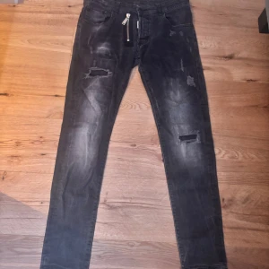 Svarta Dsquared2 skinny jeans med dragkedja - Snygga svarta jeans från Dsquared2 med slitna detaljer och trasiga partier på benen. Modellen är skinny fit med en cool dragkedjedetalj framtill och broderad D-logga på bakfickan. Jeansen har en tvättad look och klassiska fem fickor.                                      Storlek M men passar som S