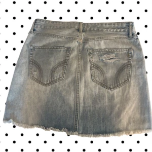 jeanskjol från Hollister - Ljusblå  jeanskjol från Hollister med slitna detaljer och fransad nederkant. Klassisk femficksmodell med dragkedja och knapp framtill. Perfekt för dig som gillar en avslappnad och trendig stil.