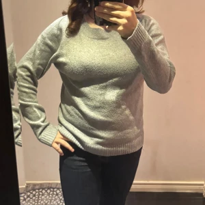Grå stickad tröja Vero Moda - Mysig grå stickad tröja från Vero Moda i storlek S. Tröjan har rund hals, ribbade muddar vid ärmslut och nederkant samt långärmad passform. Perfekt för kyliga dagar och enkel att matcha med jeans eller kjol.