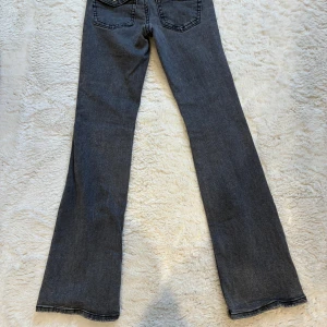 Grå bootcut jeans från Gina Tricot - Snygga grå jeans från Gina Tricot i modellen Perfect Jeans. De har bootcut-ben, klassiska fem fickor och coola detaljer med knappar på bakfickorna. Jeansen är i stretchigt denim och har dragkedja framtill. Hör av er om du har några frågor.💗