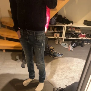 Replay Anbass med slitningar - Säljer ett par Replay Anbass jeans i blå denim med slitna detaljer och snygg tvätt. Modellen har smal passform och klassisk femficksdesign. Perfekta för dig som gillar en modern och avslappnad stil.