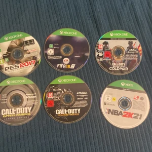 Xbox One Spelpaket (6 spel) - Paket med 6 Xbox One-spel: Call of Duty Black Ops Cold War, Infinite Warfare, Advanced Warfare, PES 2017, FIFA 18 och NBA 2K21. Skivorna ser ut att vara i gott skick utan synliga repor. Perfekt för sport- och actionälskare!