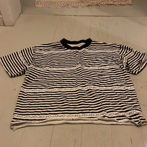 Randig svartvit t-shirt från POLAR - Säljer en svartvit t-shirt från POLAR i storlek S. T-shirten har ett coolt randigt mönster med logotypen tryckt i rader och en svart ribbad krage. Modellen är kortärmad och har en loose passform, perfekt för en chill och avslappnad stil.