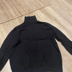 Svart polotröja från H&M Basics - Svart polotröja från H&M Basics i storlek L. Tröjan har lång ärm och hög polokrage, perfekt för att hålla värmen. Materialet är mjukt och känns skönt mot huden, och den har en klassisk, enkel design som funkar till många olika stilar.