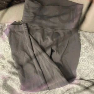 Grå höga seamless leggings Aim'n - Snygga grå seamless leggings från Aim'n med hög midja och ribbad linning. Materialet är stretchigt och bekvämt, perfekt för träning eller chill. Diskret Aim'n-logga upptill och små perforeringar längs benen för extra ventilation.