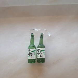 Gröna soju-örhängen - Unika örhängen formade som små soju-flaskor Hängande modell med silvriga krokar och transparenta pluppar. Perfekt för dig som vill sticka ut med ett roligt och annorlunda smycke.