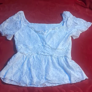 Vit spetsblus med volang - Säljer en söt vit blus med spets och volangkant. Blusen har korta puffärmar och en bred, fyrkantig halsringning. Materialet är genombruten spets med elastisk smock i ryggen för skön passform. Perfekt för dig som gillar spets 