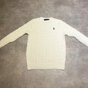 Vit kabelstickad tröja Polo Ralph Lauren - Säljer en vit kabelstickad tröja från Polo Ralph Lauren i storlek M. Tröjan har rund hals, lång ärm och den klassiska broderade loggan på bröstet. Mjuk och skön, perfekt för kyliga dagar. Passar dig som gillar stilrena och tidlösa plagg.
