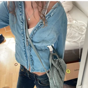 Jeansjacka med volang  - Säljer en sjukt cool ljusblå jeansjacka från isolde med dragkedja framtill och snygga volangdetaljer längs öppningen. har tajtat åt den där bak så den ska se tajtare ut men man kan annars sy om så att den blir så. Jackan har lång ärm och figurnära passform, perfekt för dig som gillar en feminin och trendig look. Fräscht och stilrent plagg att ha i garderoben.Hör av dig om du har några frågor eller funderingar 💕