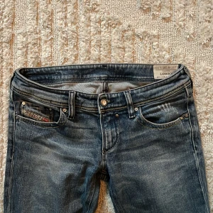 Diesel Lowky blå bootcut jeans - Snygga blå jeans från Diesel, modell Lowky, med klassisk femficksdesign och detaljerade nitar. Jeansen har låg midja och smal passform med raka ben. Materialet är slitstarkt denim i bomull och de har coola slitningar för en trendig look.