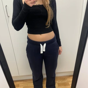 Svart croppad topp från FB Sister - Säljer en svart, croppad långärmad topp från FB Sister i ribbad bomull. Toppen har en liten rosett vid halsringningen och en smal passform som sitter snyggt på kroppen. Perfekt för dig som gillar stilrena basplagg med en söt detalj.