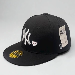 Svart New Era Yankees keps 59FIFTY - Svart keps från New Era med Yankees-logga i vitt framtill och ett litet broderat hjärta. På sidan finns ett färgglatt World Series 1996-märke. Platt skärm och klassisk 59FIFTY-modell. Undersidan av skärmen är grå. Perfekt för dig som gillar sportig stil.