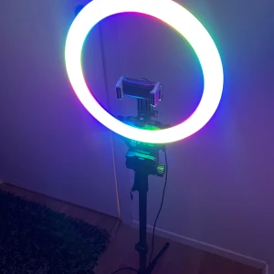 RGB Ring Light med stativ och fjärrkontroll - RGB ring light med justerbart stativ och mobilhållare. Flera ljuslägen, inklusive färgade och vitt ljus. Fjärrkontroll för iOS/Android medföljer. Perfekt för foto, video och streaming. Mycket fint skick, inga synliga defekter.