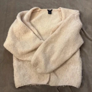 Beige stickad kofta från Lindex - Mysig beige stickad kofta från Lindex i storlek S. Koftan har en mjuk och fluffig känsla, långärmad design och en öppen front utan knappar. Perfekt att slänga på sig när det är lite kyligt ute. Passar dig som gillar en enkel och chill stil.