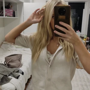 Beige stickad kofta från 157 - Snygg beige stickad kofta från 157 med korta ärmar och krage. Koftan har två knappar framtill och en mjuk, ribbad kant vid nederdelen. Perfekt att slänga över en topp för en chill och stilren look.