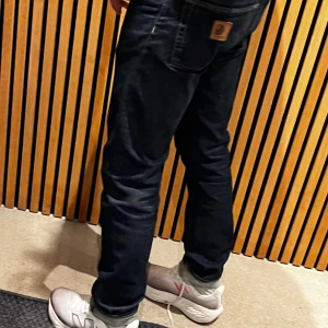 Carhartt Klondike mörkblå jeans 29/32 - Mörkblå jeans från Carhartt, modell Klondike Pant. Klassisk femficksdesign med kontrastsömmar och Carhartt-logga i läder på bakfickan. Rakt snitt och normal passform, tillverkade i bomull med lite elastan för extra komfort.