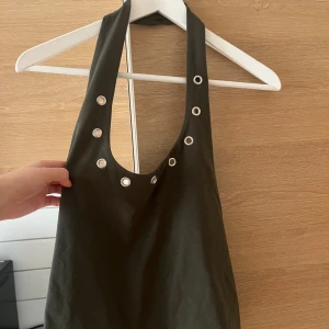 Oanvänd halterneck topp - Snygg halterneck topp med coola silver detaljer. Väldigt fin och helt ny med prislapp kvar. Tyvärr inte kommit till användning! Färgen är mer Khaki. Köpte för 299kr nypris.