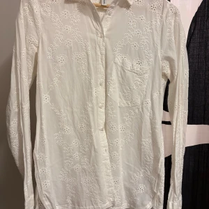 Vit broderad skjorta Soyaconcept - Snygg vit skjorta från Soyaconcept med broderade blommor och hålmönster över hela plagget. Skjortan har klassisk krage, knappar framtill, bröstficka och slits i sidorna. Långärmad och tillverkad i mjuk bomull som känns skön mot huden.