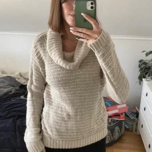 Beige stickad polotröja med lös krage - Mysig beige stickad polotröja med bred, lös krage och lång ärm. Tröjan har ett grovt stickat mönster och ribbad vid ärmslut och nederkant. Perfekt för lager-på-lager under kyliga dagar.