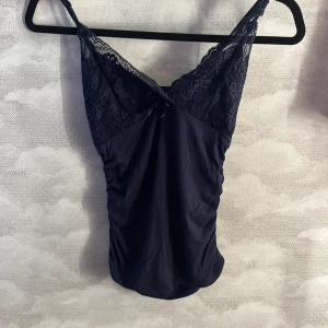 Mörkblå spetsdetaljerad linnetopp - Säljer en mörkblå linnetopp från Shein i storlek S. Toppen har tunna axelband, spetsdetaljer med blommönster upptill och en liten rosett framtill. Materialet är mjukt och stretchigt, perfekt för en trendig look.