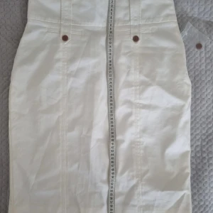 Vit långkjol  - Vit långkjol i bomullsblandning med snygga bruna knappar. Kjolen har en rak passform och är fodrad med polyester för extra komfort.  Passar för storlek S-M 