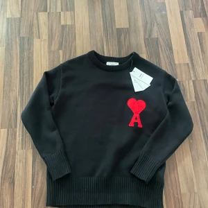 Svart stickad tröja från Ami Paris - Svart stickad tröja från Ami Paris med rund halsringning och ribbade muddar. På bröstet finns ett rött broderat hjärta med bokstaven A. Perfekt för dig som gillar stilrena plagg med en twist.
