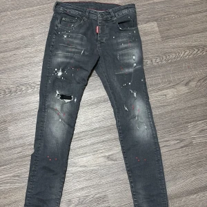Dsquared2 svarta skinny jeans med färgstänk - Svarta skinny jeans från Dsquared2 med coola slitningar, färgstänk i vitt och rött samt en tydlig logga på fickan. Jeansen har fem fickor, låg midja och en smal passform. Perfekta för dig som gillar en edgy streetstil.