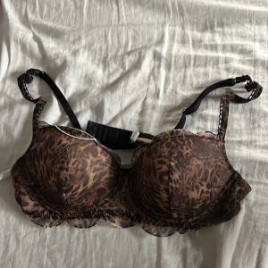 Leopardmönstrad bh med volang - Säljer en snygg bh med leopardmönster i bruna och svarta toner. Toppen har justerbara svarta axelband och en söt volangkant nedtill. Perfekt för dig som vill sticka ut med en djurisk vibe.