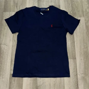 Marinblå t-shirt från Polo Ralph Lauren - Snygg marinblå t-shirt från Polo Ralph Lauren med klassisk passform. Jag säljer den för att jag Bhöver pengar just nu och jag kan inte gå ner mer!
